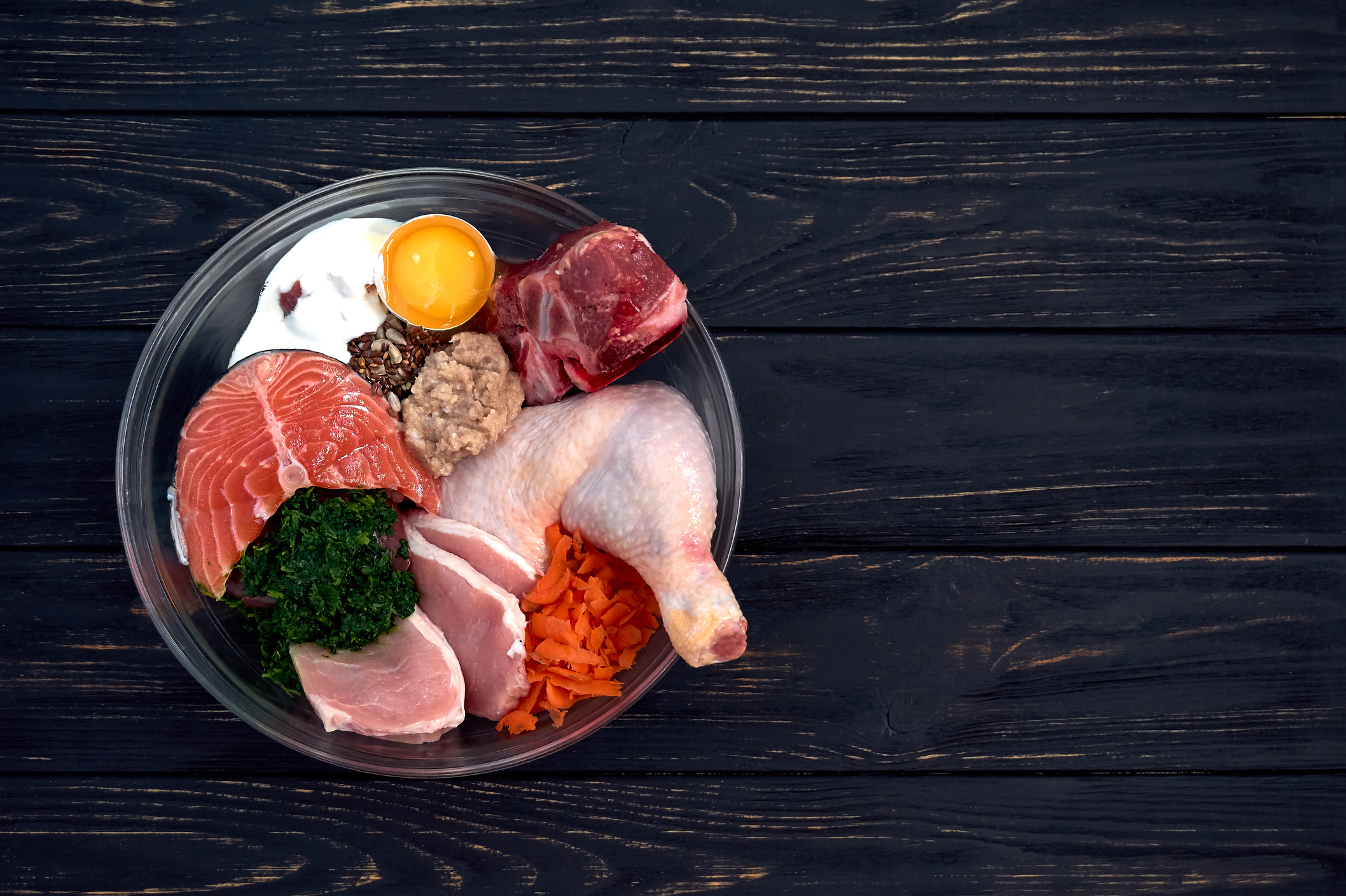 Natural Raw organic dog food in bowl on black wooden background. BARF dog diet. Copy space.